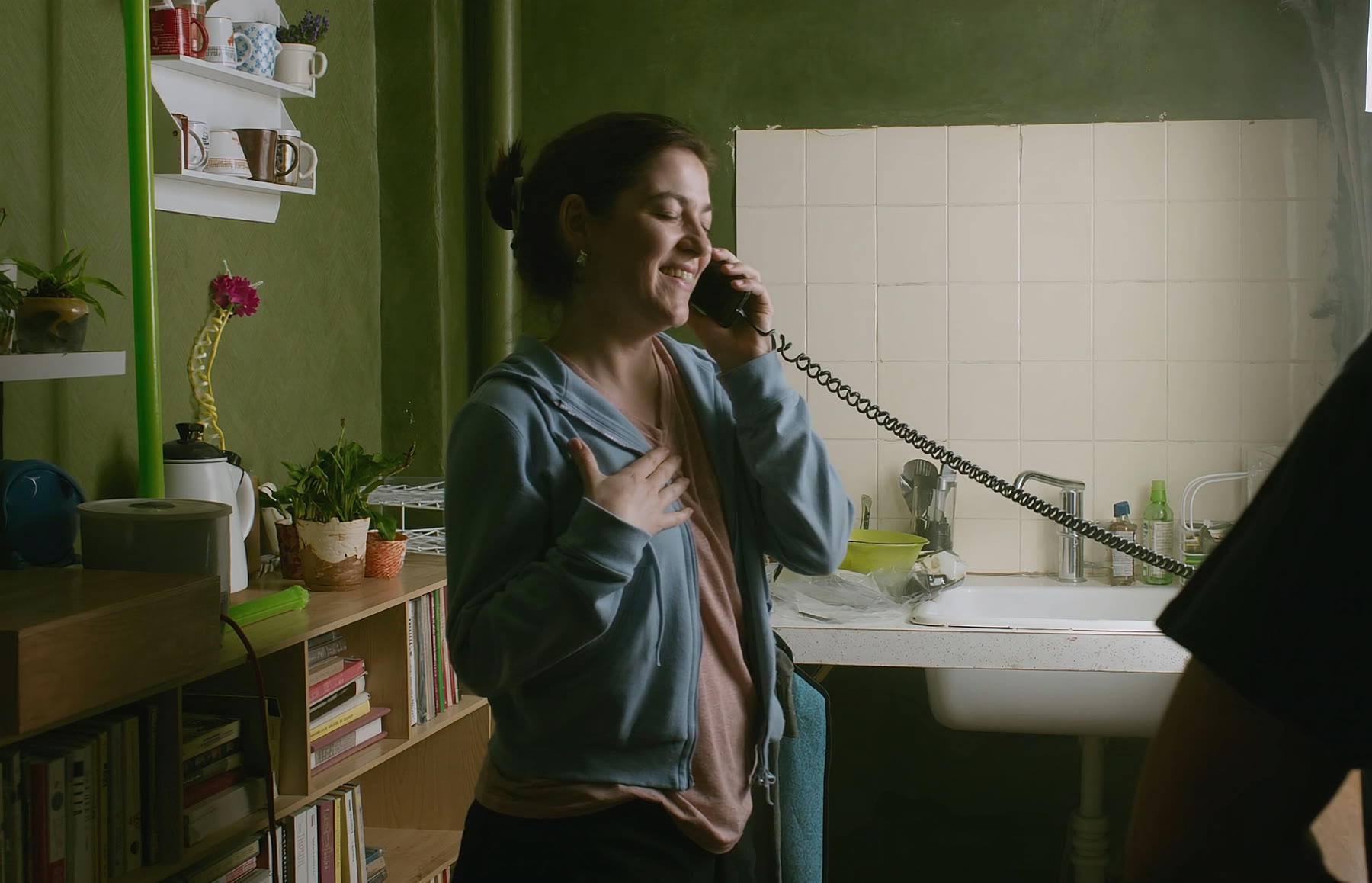 Žena v kuchyni si pri telefonáte s úľavou kladie ruku na srdce